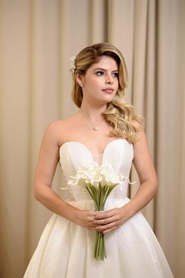 Noiva com penteado lateral segurando buquê de copos-de-leite